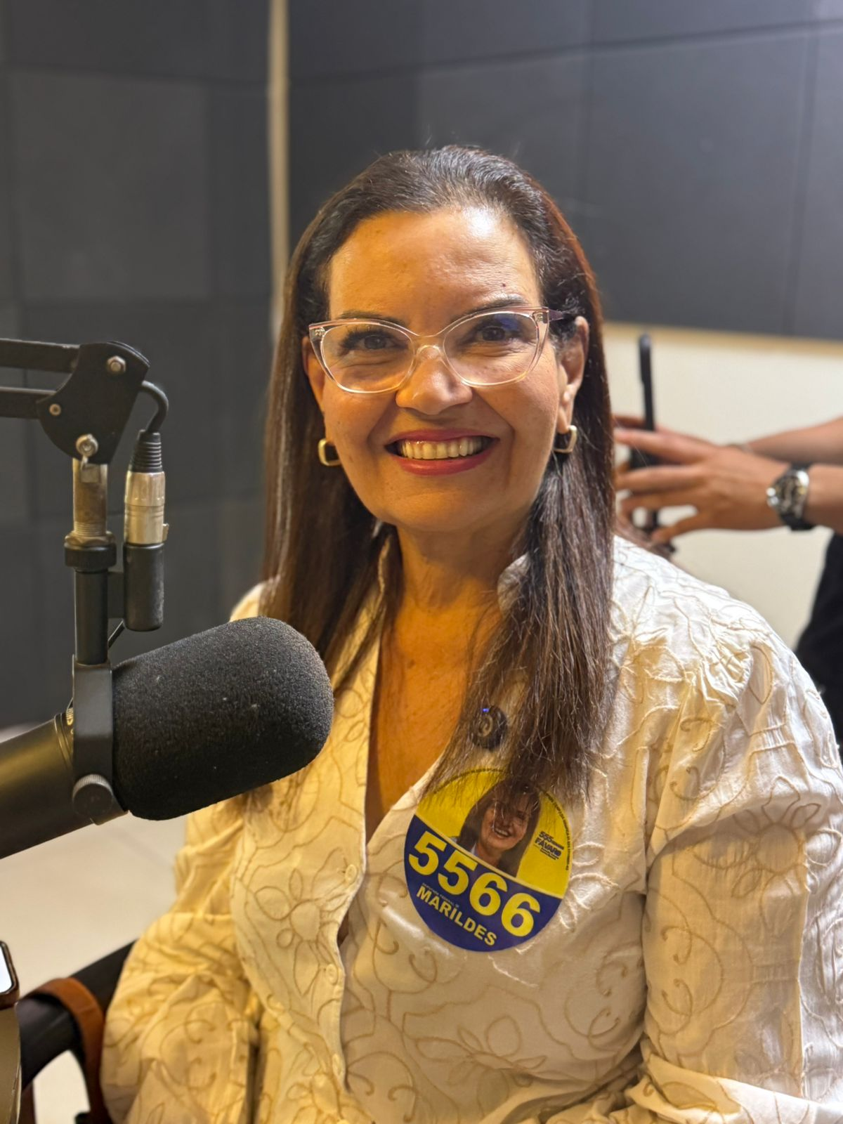 Marildes Ferreira sorrindo diante do microfone durante entrevista de rádio